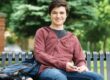 Male college student sitting on bench with back pack