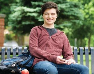 Male college student sitting on bench with back pack