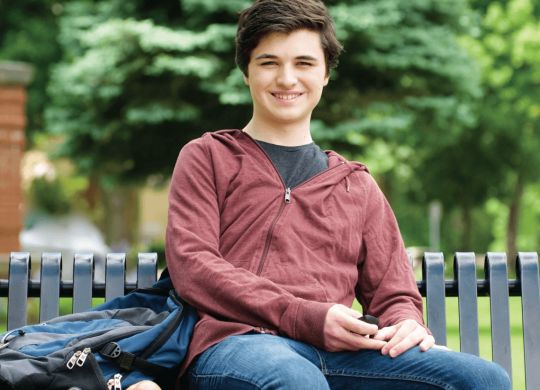 Male college student sitting on bench with back pack