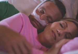 Man wearing CPAP face mask while dozing with his wife in bed