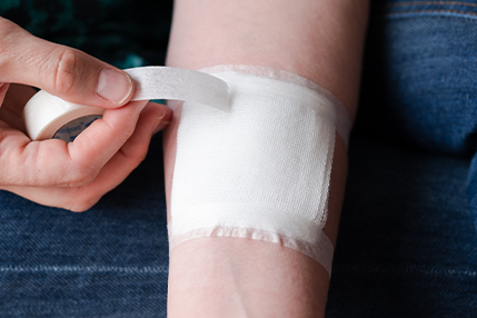 Doubek-WoundCare101 Person wrapping their wound with a gauze and taping it with white tape