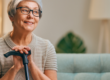 Older woman sitting on couch smiling with her hands on a cane