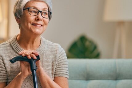 Older woman sitting on couch smiling with her hands on a cane