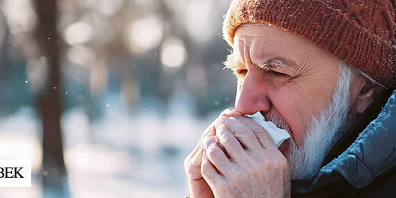 Man outside in the winter holding a tissue to his nose and over his mouth