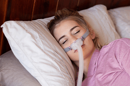 Doubek-CPAPImproveLife Woman lying down on bed with CPAP mask on her face